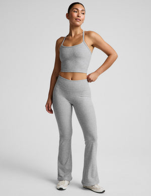 Woman wearing a gray racerback cropped tank top and mid rise bootcut pants against a plain background. 
