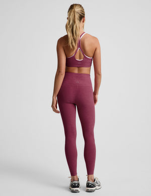 A woman is shown from the back wearing a matching athletic set consisting of a heathered dusty rose sports bra and high-waisted leggings, paired with black and white sneakers, against a light gray studio background.
