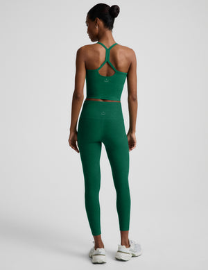 Woman wearing a green racerback cropped tank top and green high-waisted midi leggings against a plain background. 