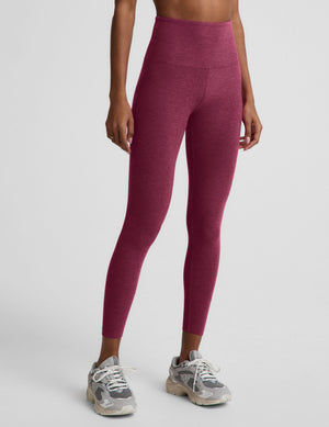 A model wearing high-waisted heathered burgundy leggings and gray athletic sneakers, shown from the waist down against a light gray studio background.