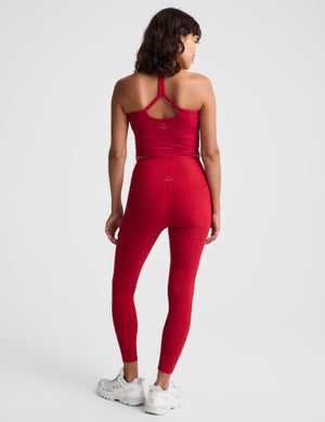 A woman shown from the back wearing a matching red activewear set consisting of a strappy tank top and high-waisted leggings, paired with white sneakers, against a light gray studio background.