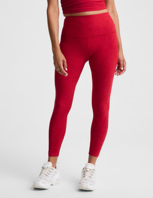 A model wearing high-waisted red leggings and white sneakers, shown from the waist down against a light gray studio background.