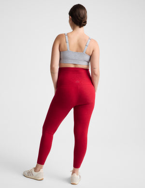 Pregnant woman red maternity leggings against a plain background. 