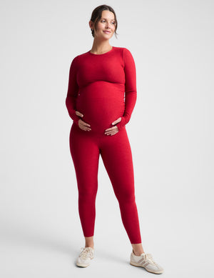 Pregnant woman wearing a red long sleeve and red maternity leggings against a plain background. 