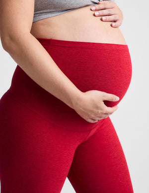 Pregnant woman red maternity leggings against a plain background. 
