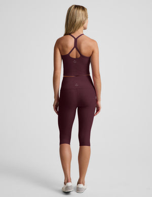 A woman shown from the back wearing a matching burgundy activewear set consisting of a cropped tank and high-waisted capri leggings, photographed against a light gray studio background.