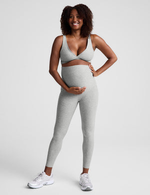 Pregnant woman wearing a gray maternity bra and gray maternity leggings against a plain background. 
