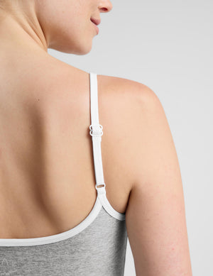 Close-up back view of a woman wearing a white adjustable underwire bra strap with a buckle, over a heather gray tank top, against a light gray studio background.