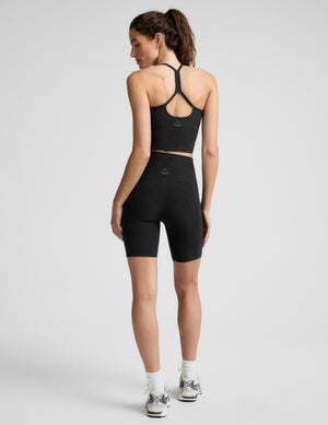 A woman modeling a black athletic crop top and matching high-waisted black biker shorts against a light gray studio background.