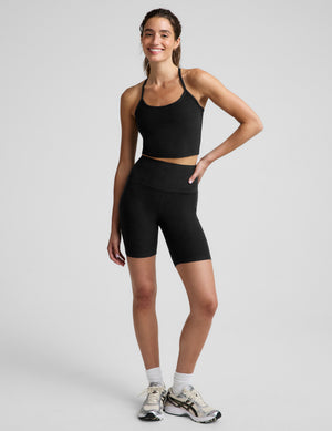 A woman modeling a black athletic crop top and matching high-waisted black biker shorts against a light gray studio background.