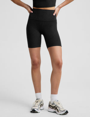 A woman modeling a black athletic crop top and matching high-waisted black biker shorts against a light gray studio background.