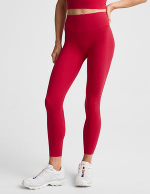 A model wearing bright red high-waisted leggings and white athletic sneakers, shown from the waist down against a light gray studio background.
