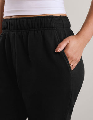 Close-up of a person wearing black sweatpants with a side pocket, with a hand resting in the pocket.