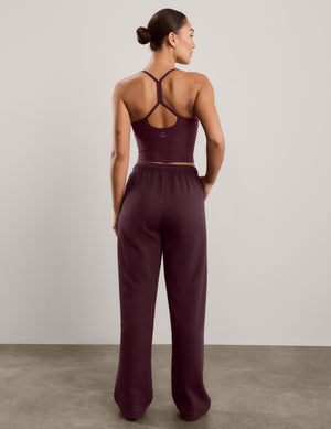 A woman modeling a matching two-piece lounge set consisting of a dark burgundy camisole top and matching wide-leg sweatpants, standing against a neutral studio background.