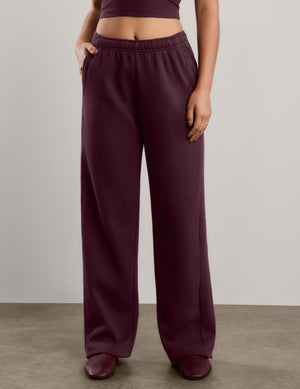 A woman modeling a matching two-piece lounge set consisting of a dark burgundy camisole top and matching wide-leg sweatpants, standing against a neutral studio background.