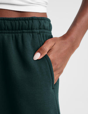 Close-up of a person wearing dark forest green sweatpants, showing the elastic waistband, side pocket, and hand resting in the pocket.