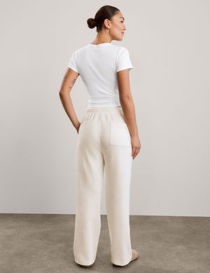 A woman modeling a white short-sleeve cropped top and off-white wide-leg sweatpants against a neutral studio backdrop.