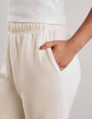 A woman modeling a white short-sleeve cropped top and off-white wide-leg sweatpants against a neutral studio backdrop.