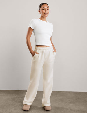 A woman modeling a white short-sleeve cropped top and off-white wide-leg sweatpants against a neutral studio backdrop.
