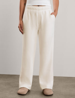 A woman modeling a white short-sleeve cropped top and off-white wide-leg sweatpants against a neutral studio backdrop.