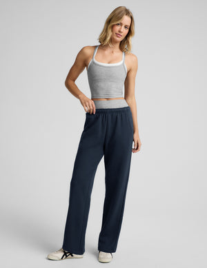 Woman wearing a gray tank top, gray biker shorts, and blue straight leg sweatpants against a plain background. 