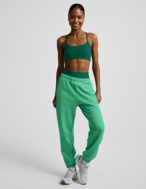 Woman wearing a green bra and green joggers against a plain background. 
