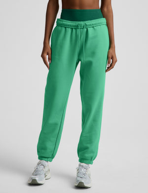 Woman wearing a green bra and green joggers against a plain background. 
