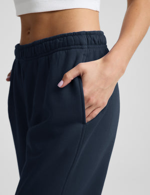 Woman wearing a white ribbed tank top and blue joggers against a plain background. 