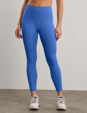 A woman modeling high-waisted blue leggings against a neutral studio backdrop.