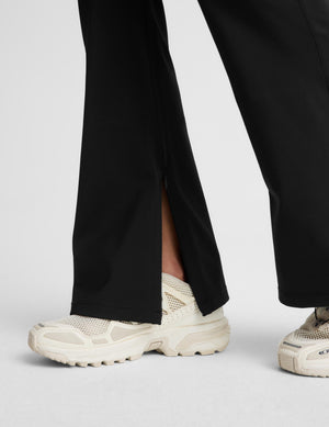 Close-up of a person wearing black wide-leg trousers with front slits and chunky off-white sneakers against a light gray studio background.