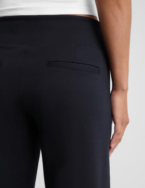 Close-up back view of a person wearing dark navy leggings or pants, showing the waistband, a welt pocket, and the back of the garment against a light gray studio background.