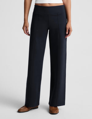 A model is shown from the waist down wearing a pair of dark navy wide-leg trousers and brown leather loafers, set against a plain light gray studio background.