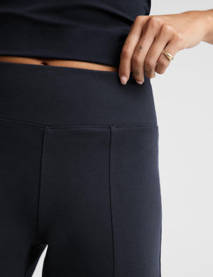 Close-up of a model wearing dark navy athletic leggings, showing the waistband and front seam, with a hand resting near the waist against a light gray background.