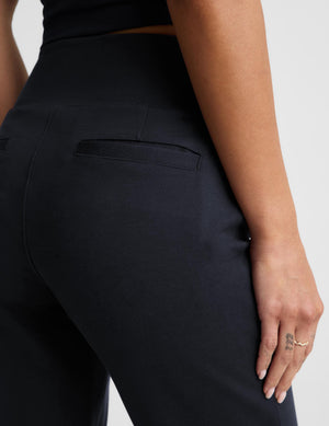 Close-up of a model wearing dark navy high-waisted trousers, showing the back pocket and side seam details against a light gray background.