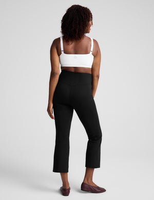 A woman shown from the back wearing black high-waisted cropped pants, a white bra, and dark brown flats against a light gray studio background.