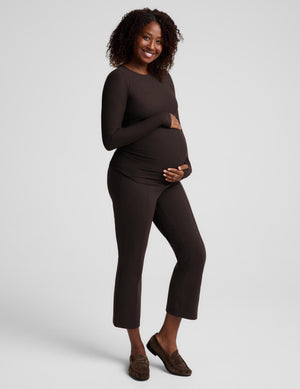 A pregnant woman modeling a dark brown long-sleeve maternity top and matching cropped pants against a light gray studio background.