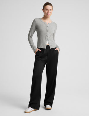 A woman modeling a gray cardigan and black wide-leg track pants against a light gray studio background.