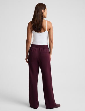 A woman shown from the back wearing a white camisole top and dark burgundy wide-leg pants against a light gray studio background.