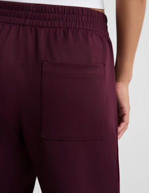 Close-up of a person wearing dark burgundy athletic jogger pants, showing the back pocket and elastic waistband against a light gray background.