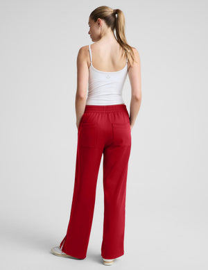 A woman shown from the back wearing red wide-leg pants and a white tank top, standing against a light gray studio background.