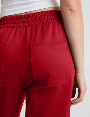 Close-up back view of a person wearing red drawstring lounge pants with a large back pocket, paired with a white cropped top against a light gray studio background.
