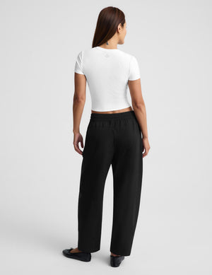 A woman modeling a white short-sleeve crop top and black wide-leg drawstring pants against a light gray studio background.