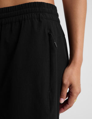 A woman modeling a white short-sleeve crop top and black wide-leg drawstring pants against a light gray studio background.