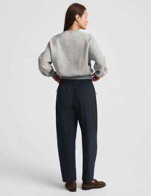 A woman modeling a light gray crewneck sweatshirt and dark navy wide-leg drawstring pants, paired with brown loafers, against a solid light gray studio background.