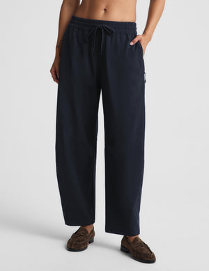 A person wearing loose dark navy drawstring pants with side pockets and brown mule loafers, photographed against a clean light gray studio background.