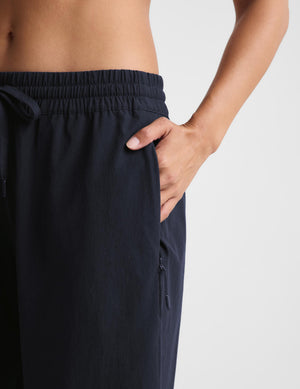 Close-up of a person wearing dark navy drawstring pants with a side pocket and zippered pocket, shown against a light gray studio background.
