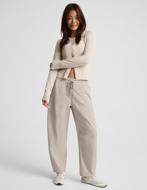 A woman modeling a matching beige set consisting of a cardigan and barrel leg drawstring pants, paired with white sneakers, against a light gray studio background.