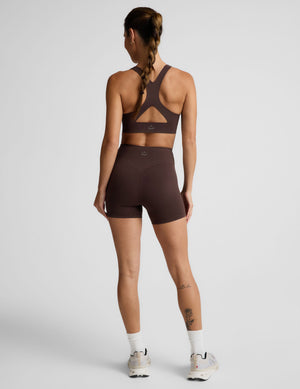 Woman wearing a brown sports bra and brown biker shorts against a plain background. 