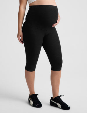 Pregnant woman wearing black pedal pushers against a plain background. 