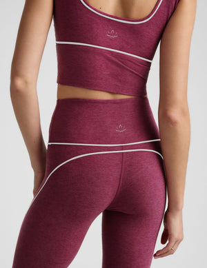 A close-up back view of a model wearing a matching burgundy activewear set with white piping and a small white Beyond Yoga logo on the back of the sports bra and leggings.